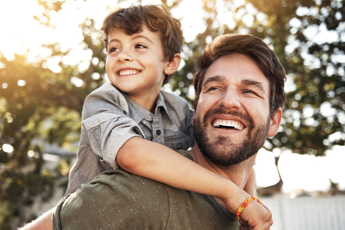 Dad with kid on his back smiling after implant dentistry in West Covina